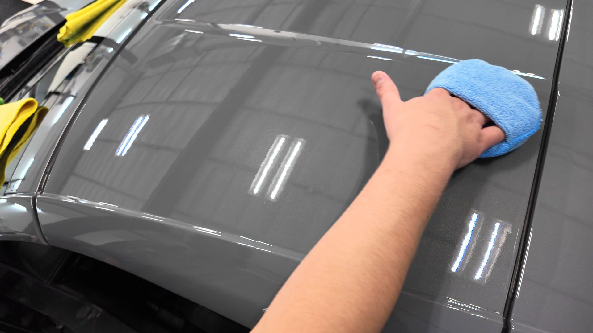 A person is cleaning the hood of a car with a blue cloth.