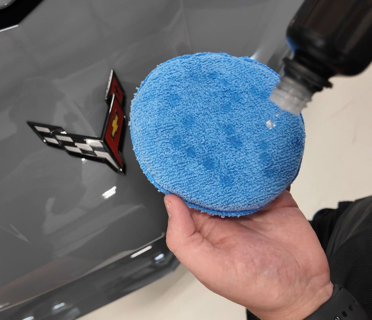 A person is polishing the hood of a blue car.