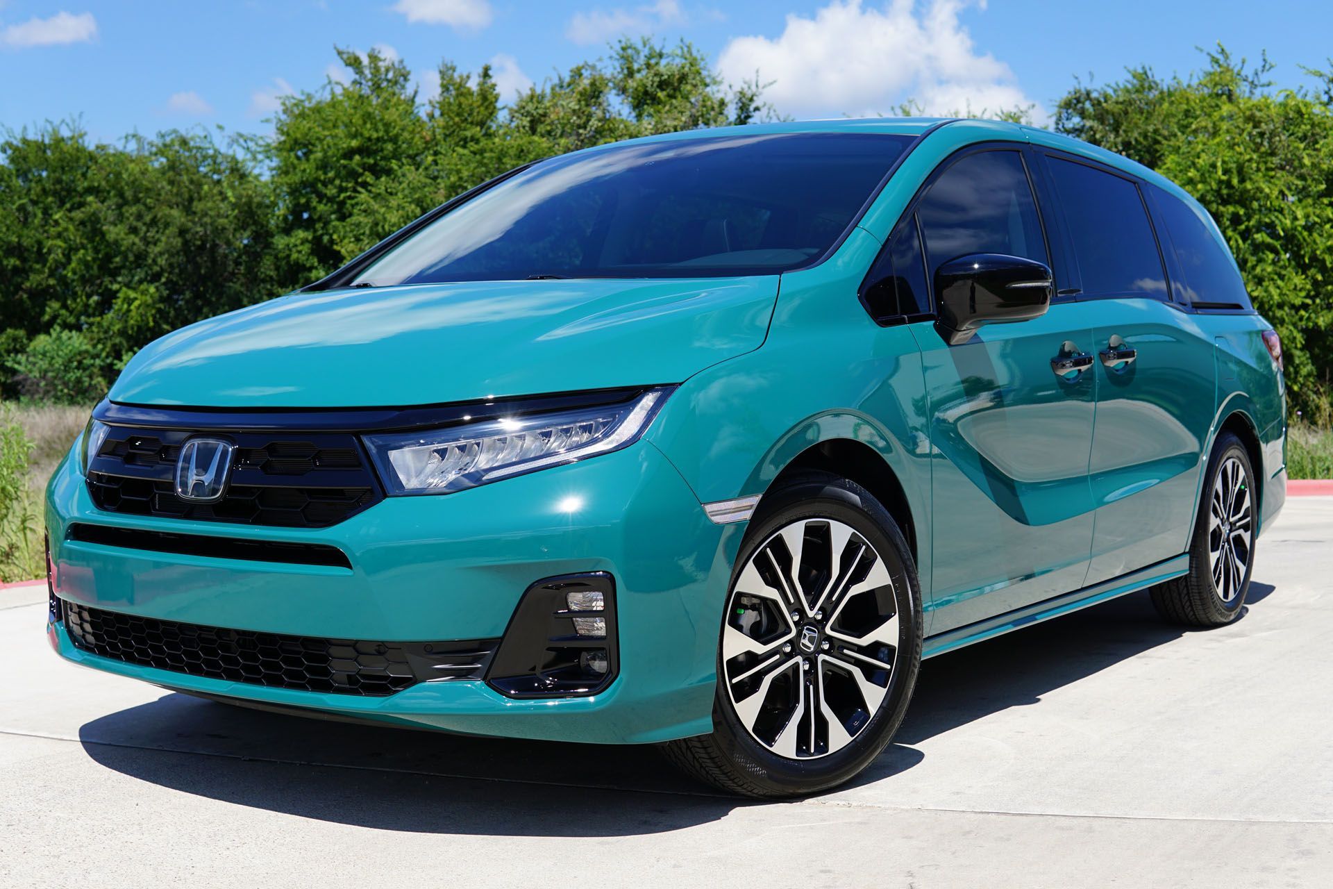 A blue honda minivan is parked on the side of the road.