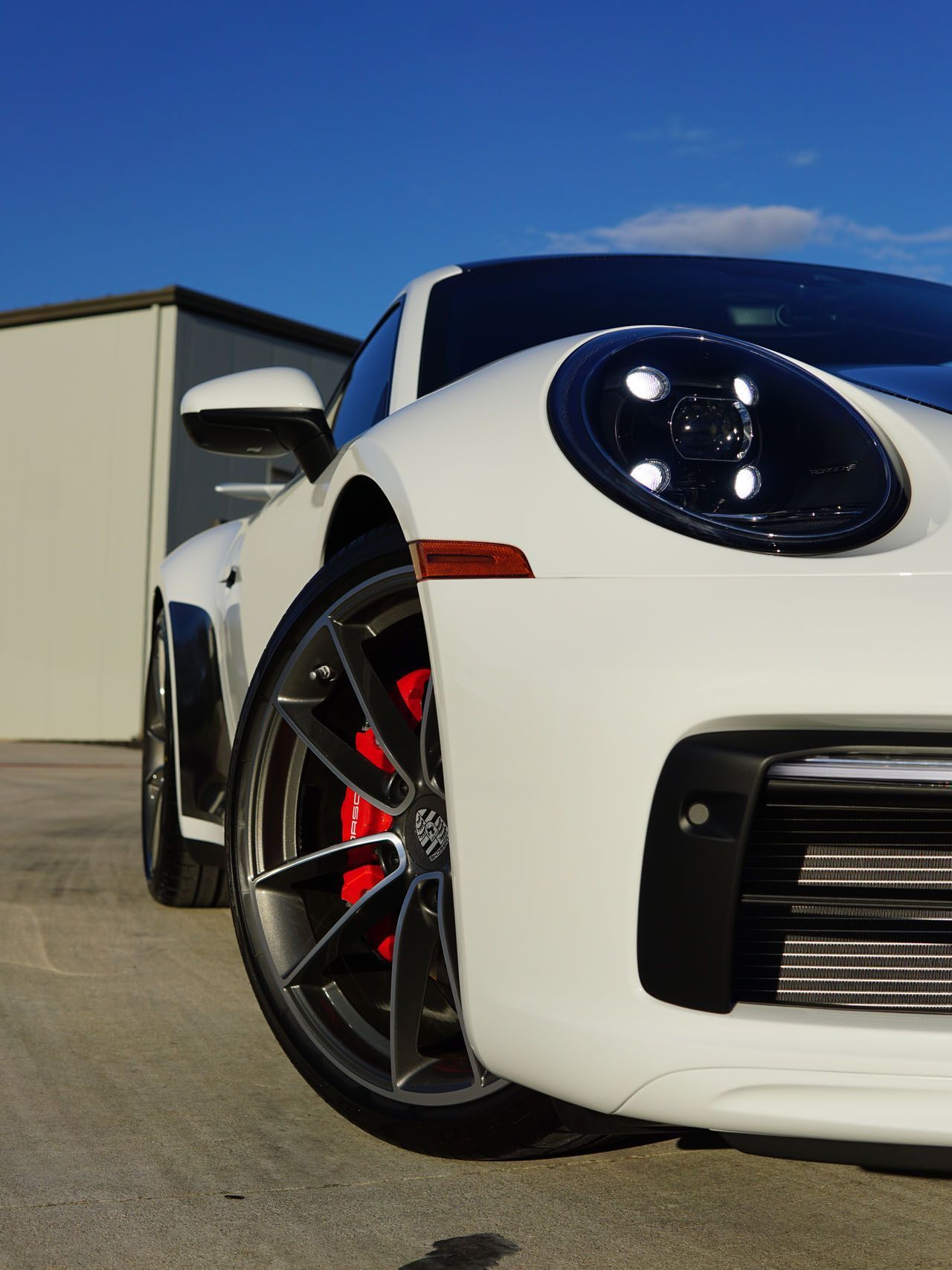 A white sports car with red brake pads is parked in front of a building.