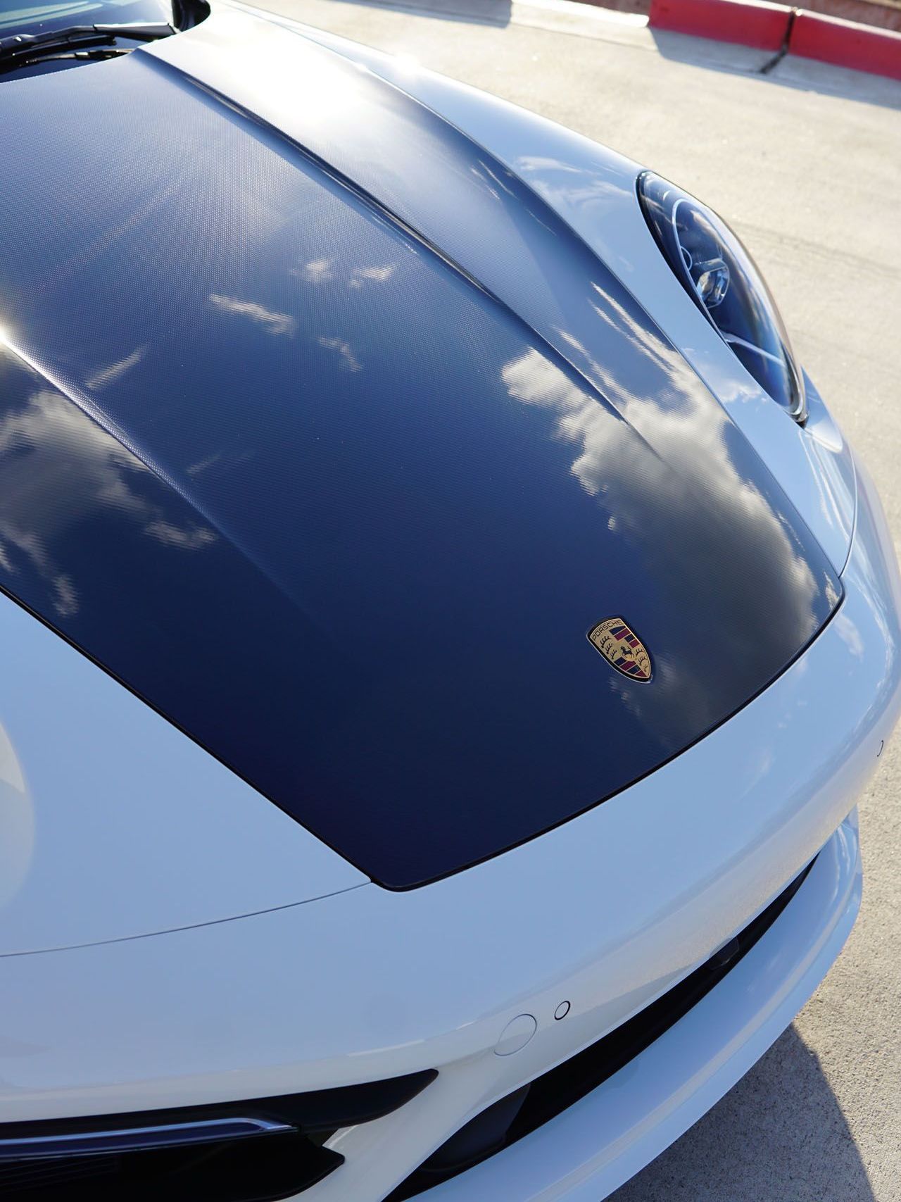 A white sports car with a black hood is parked in a parking lot