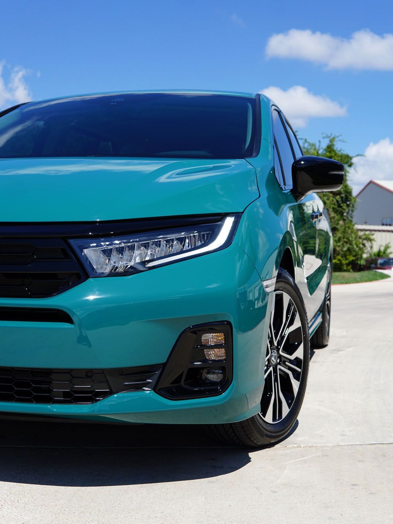 A green car is parked on the side of the road on a sunny day.