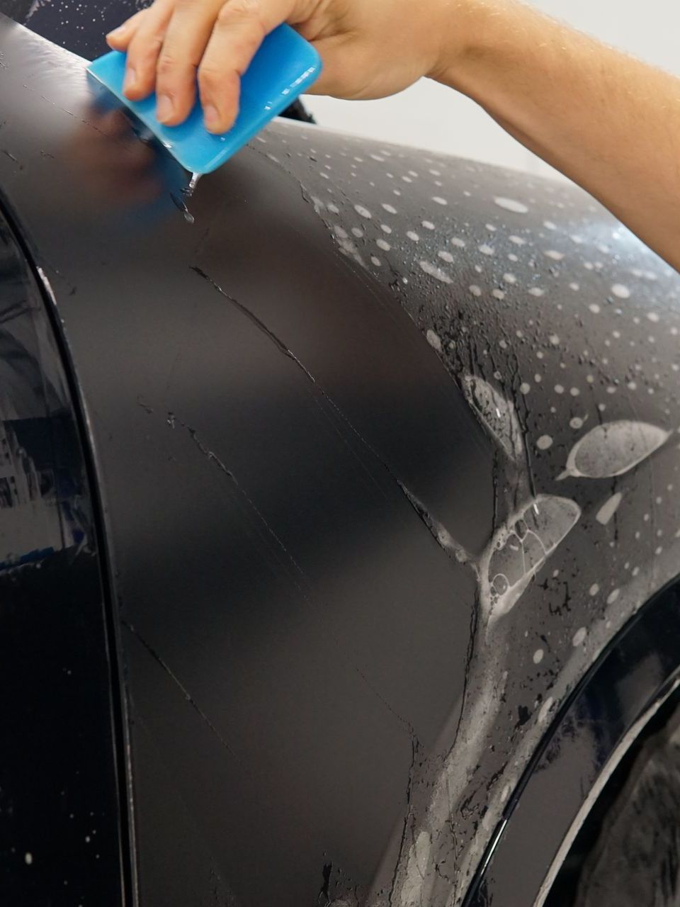 A person is cleaning a car with a blue sponge