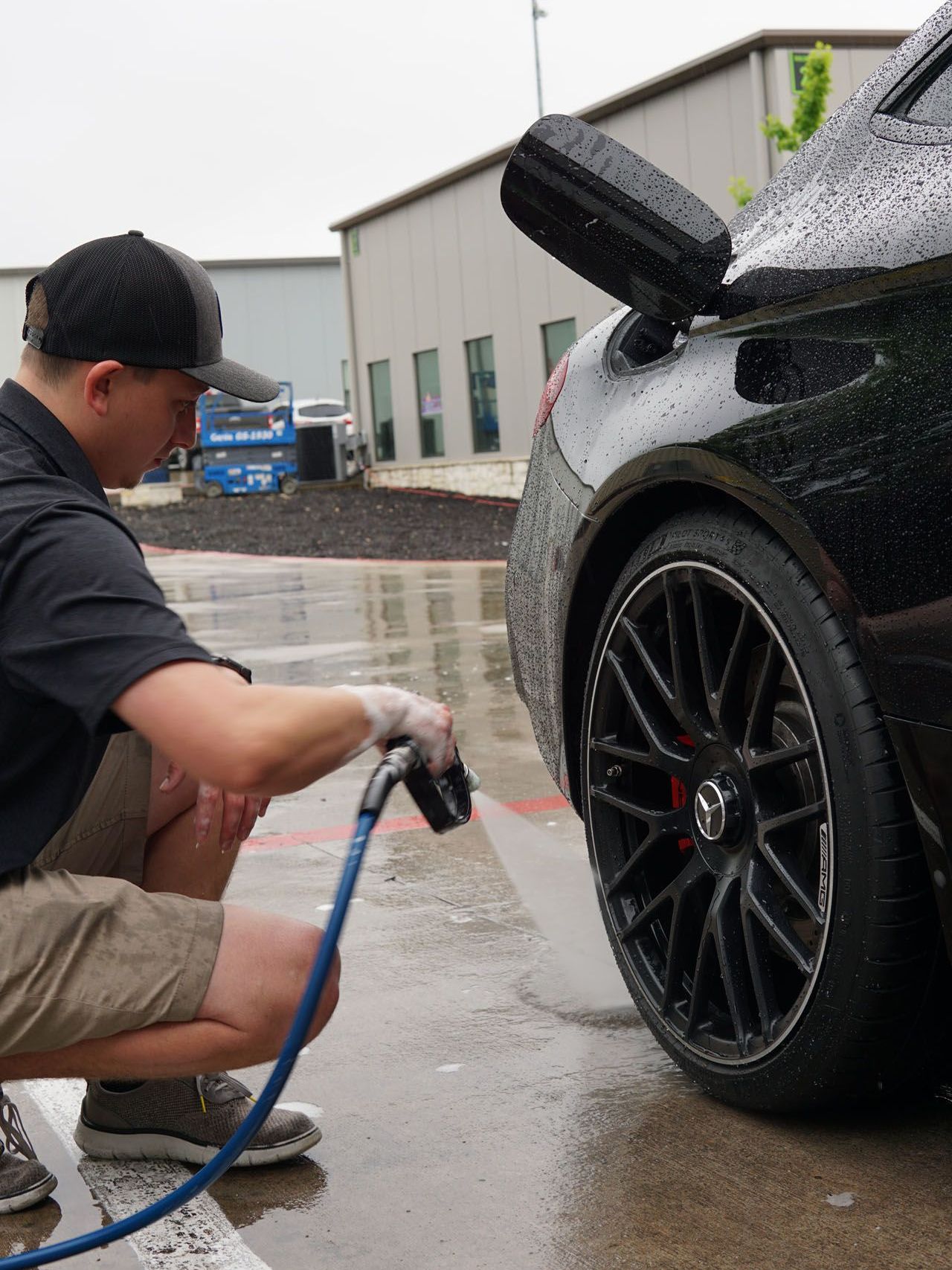 A man is kneeling down to wash a car with a hose