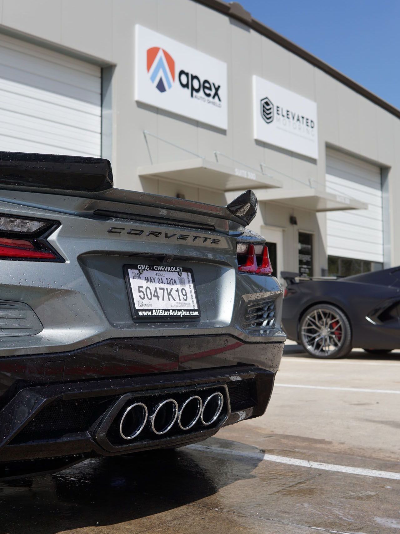 A silver corvette is parked in front of an apex building