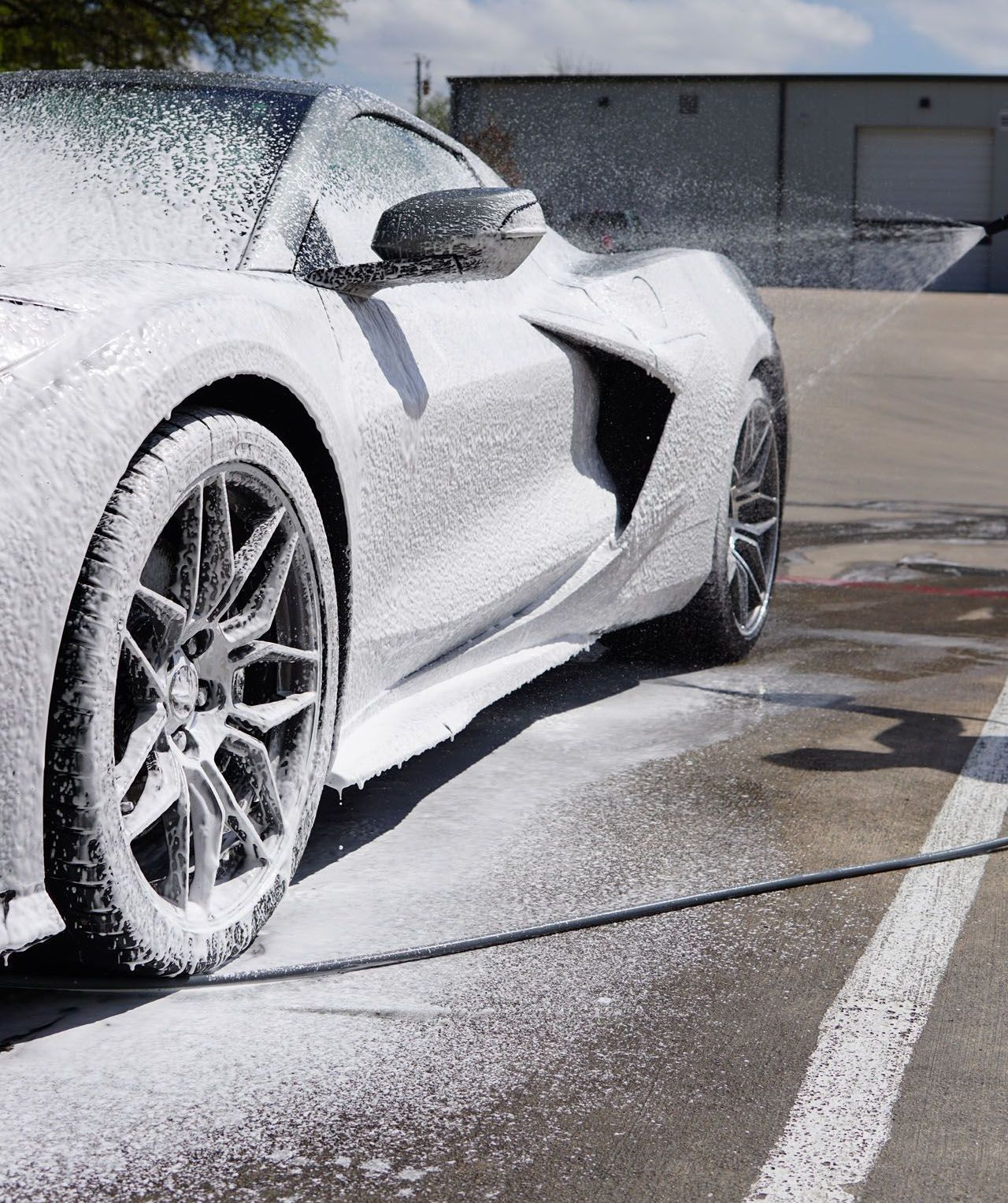 A white sports car is covered in foam in a parking lot