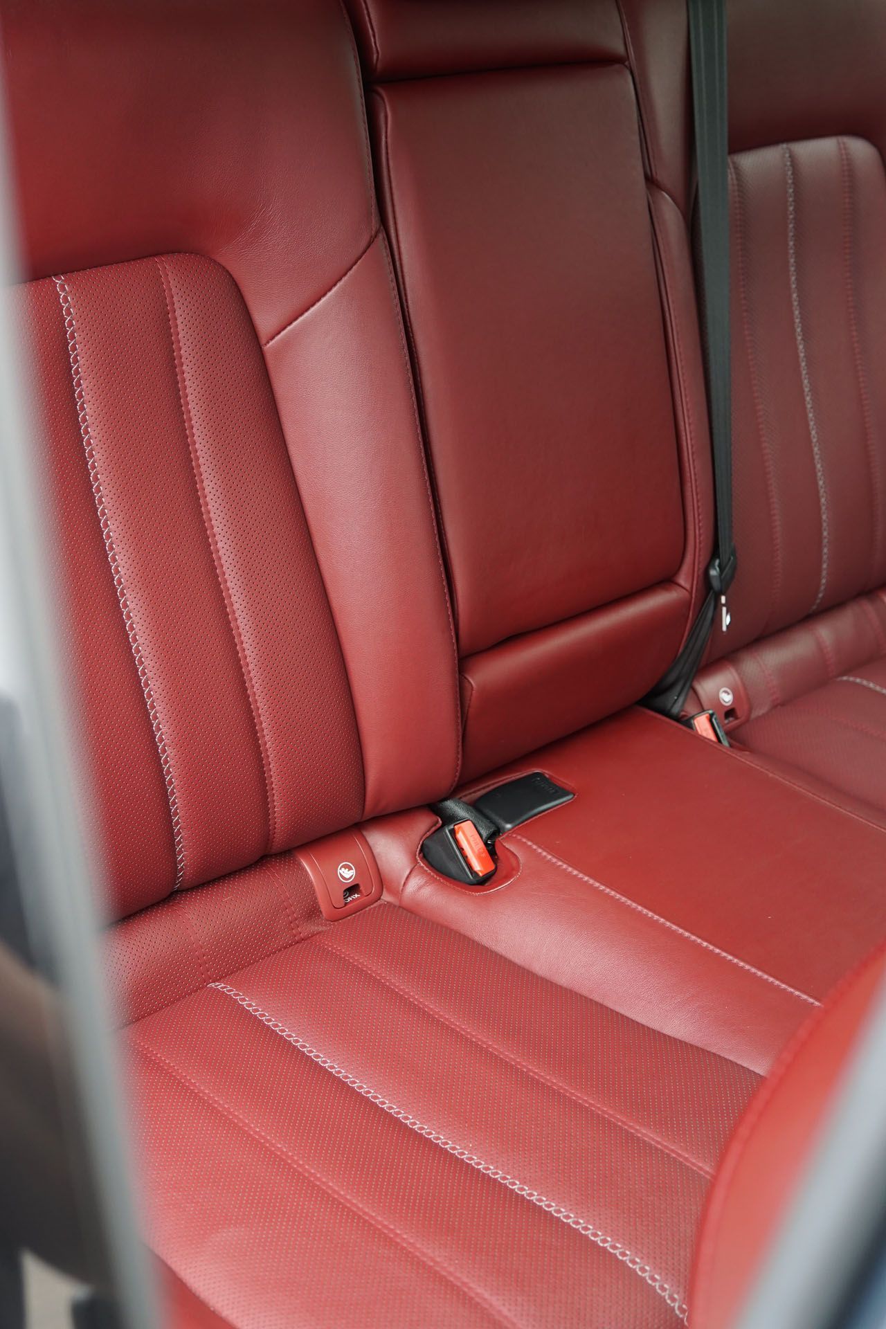 The back seat of a car is red leather and has a seat belt.