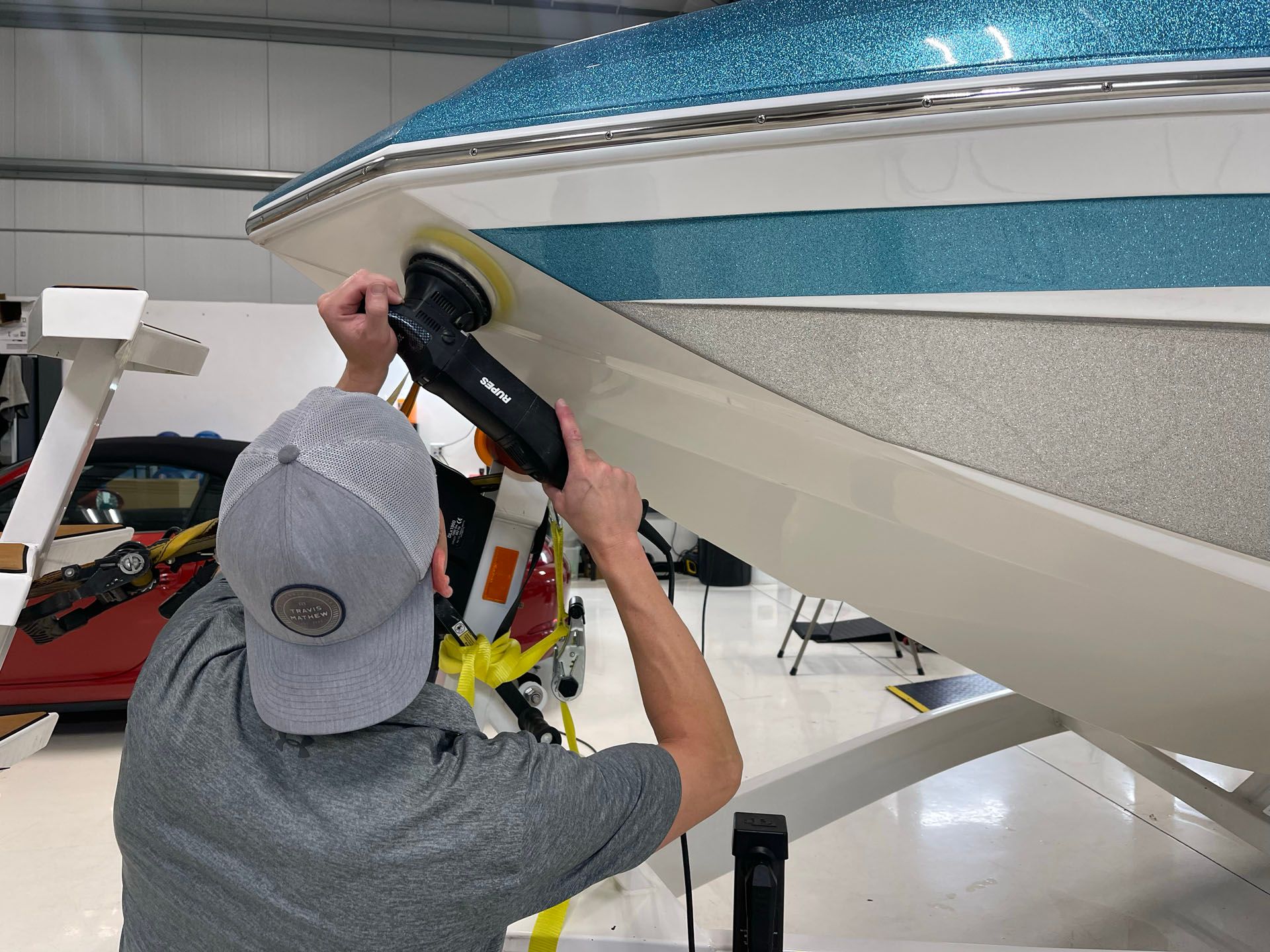 A man is polishing the side of a boat with a machine.