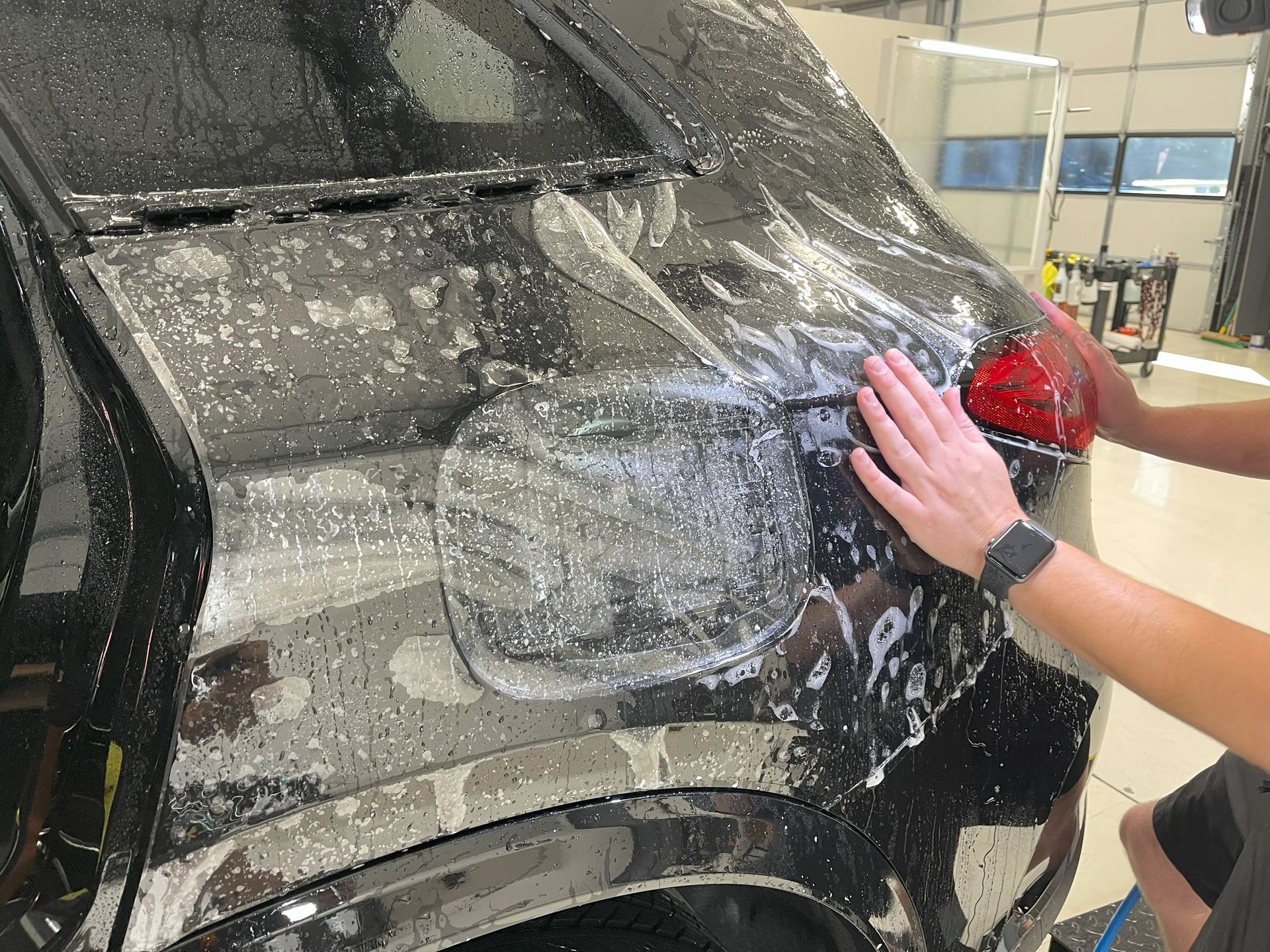 A person is covering the hood of a car with plastic wrap.