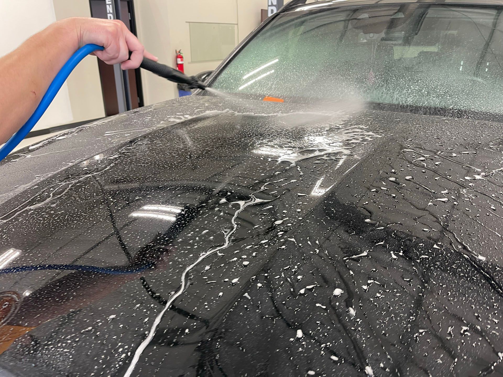 A person is washing a black car with a hose.