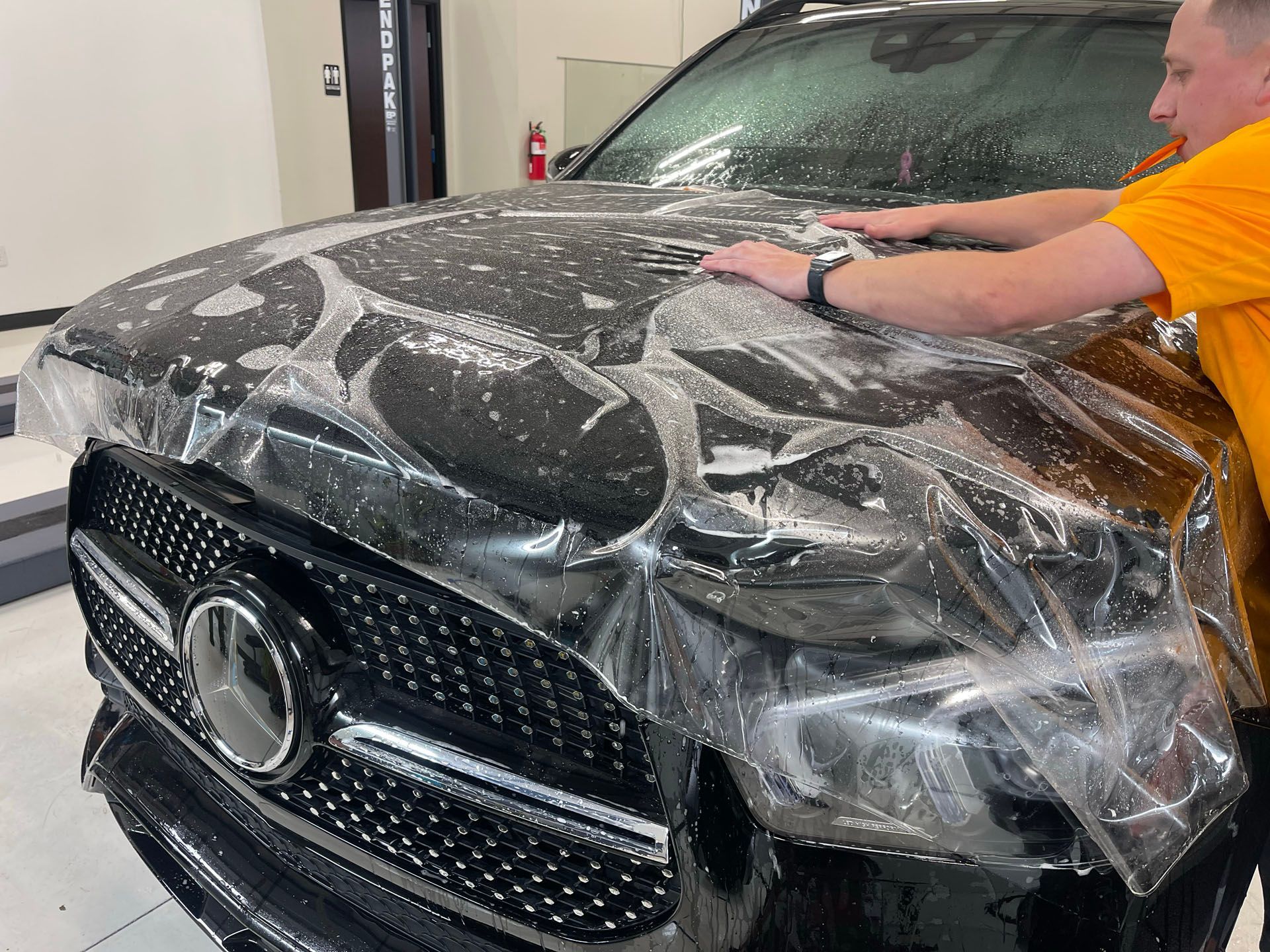 A man is wrapping a black mercedes with plastic wrap.