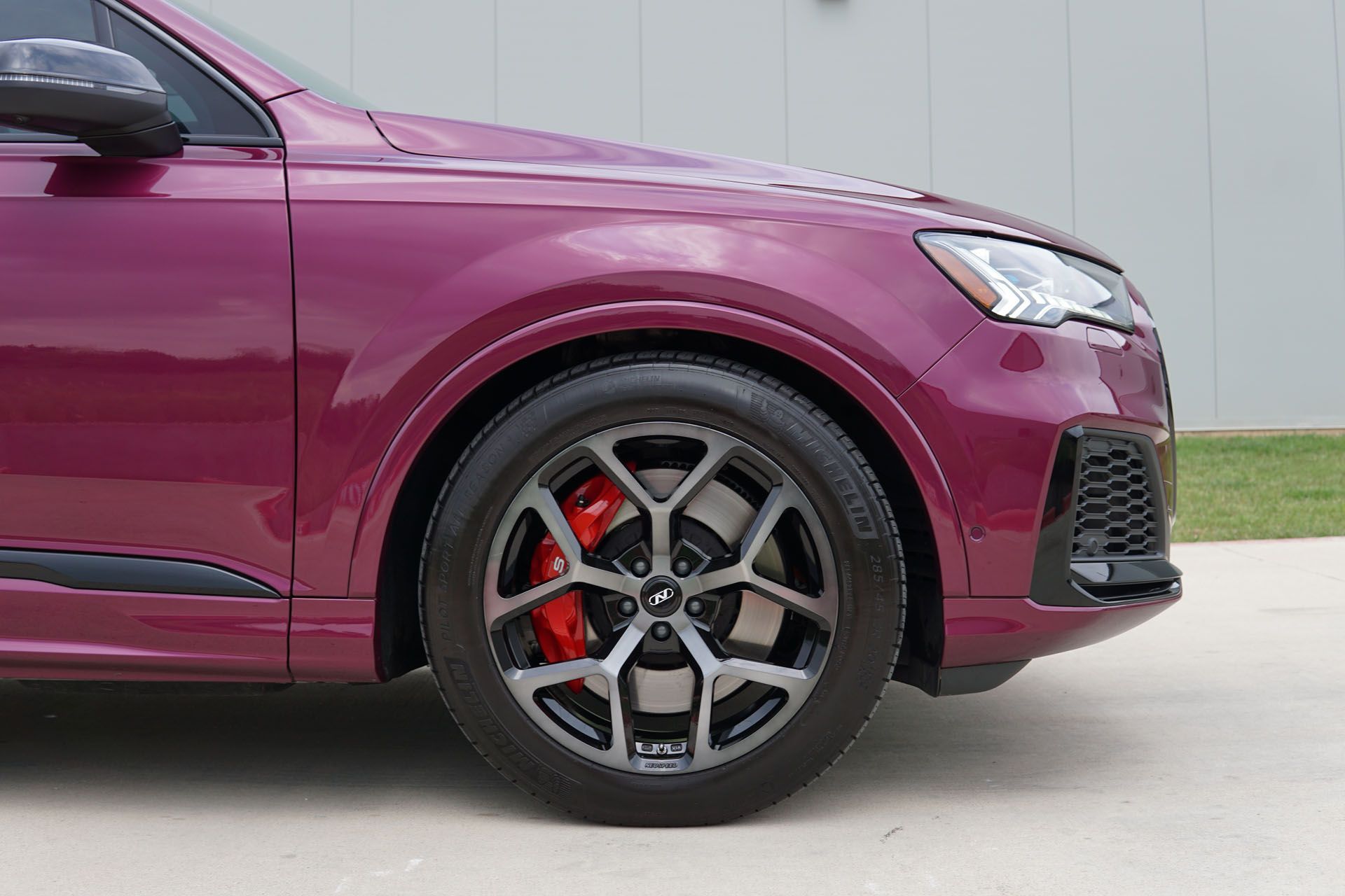 A purple car with red brake calipers is parked in front of a building.