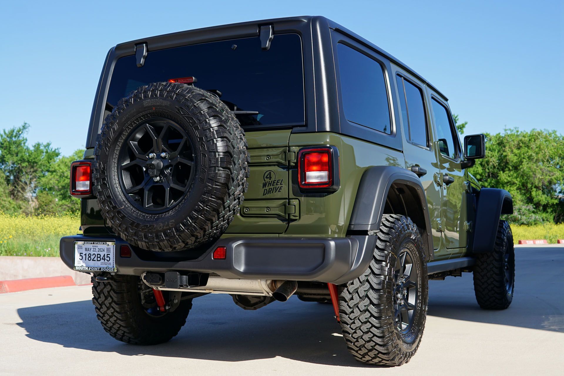 Green Jeep Wrangler with black top and spare tire, parked outdoors.