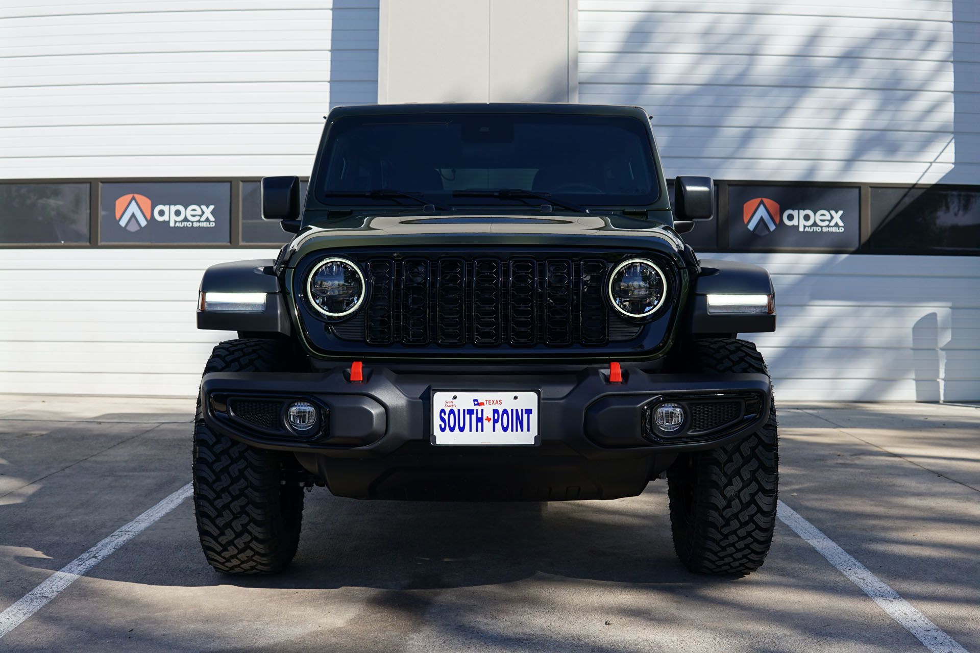 Black Jeep Wrangler, black grill, and round headlights, parked in front of a garage with Apex Solutions logos.