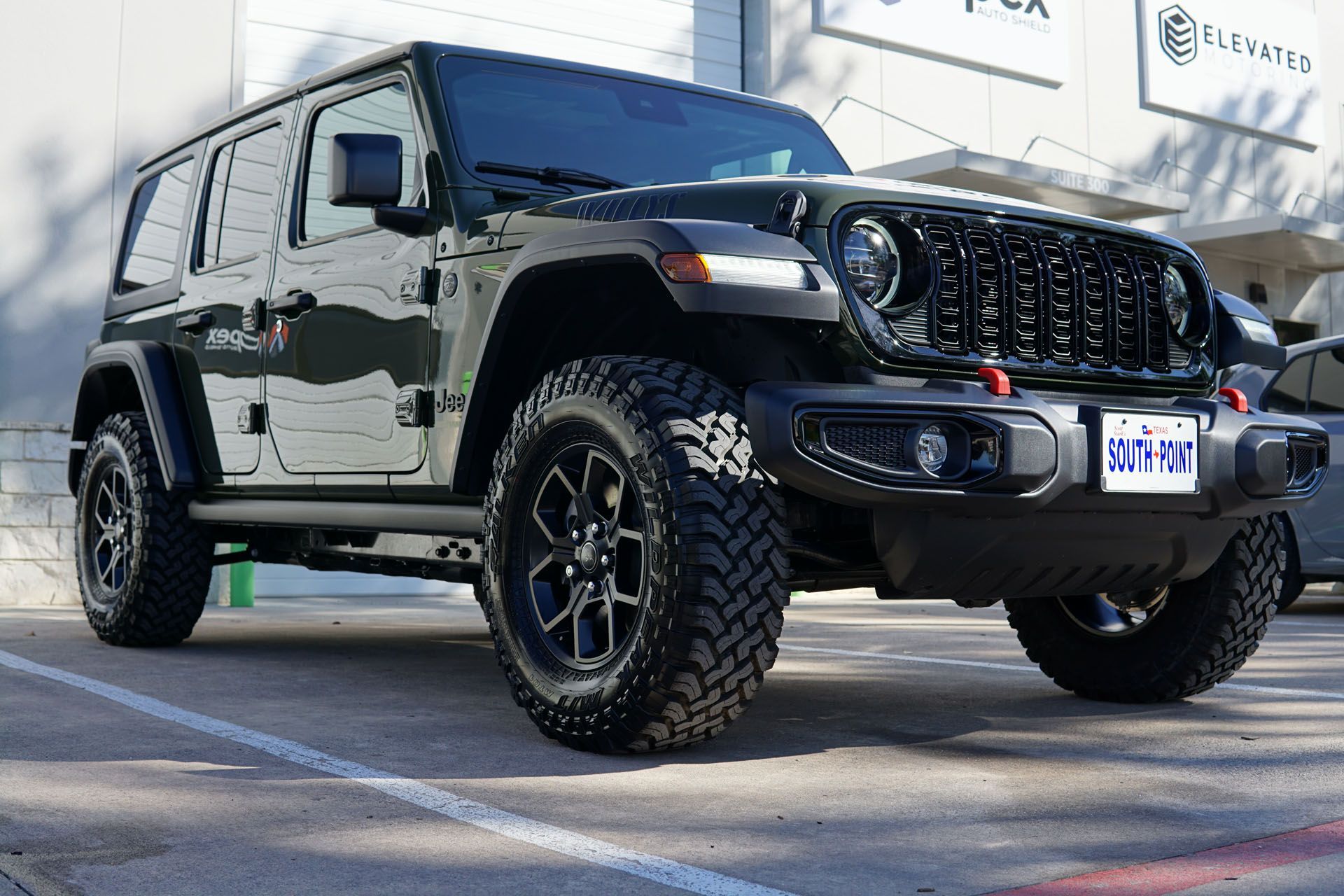 Dark green Jeep Wrangler with black rims and tires parked outside.