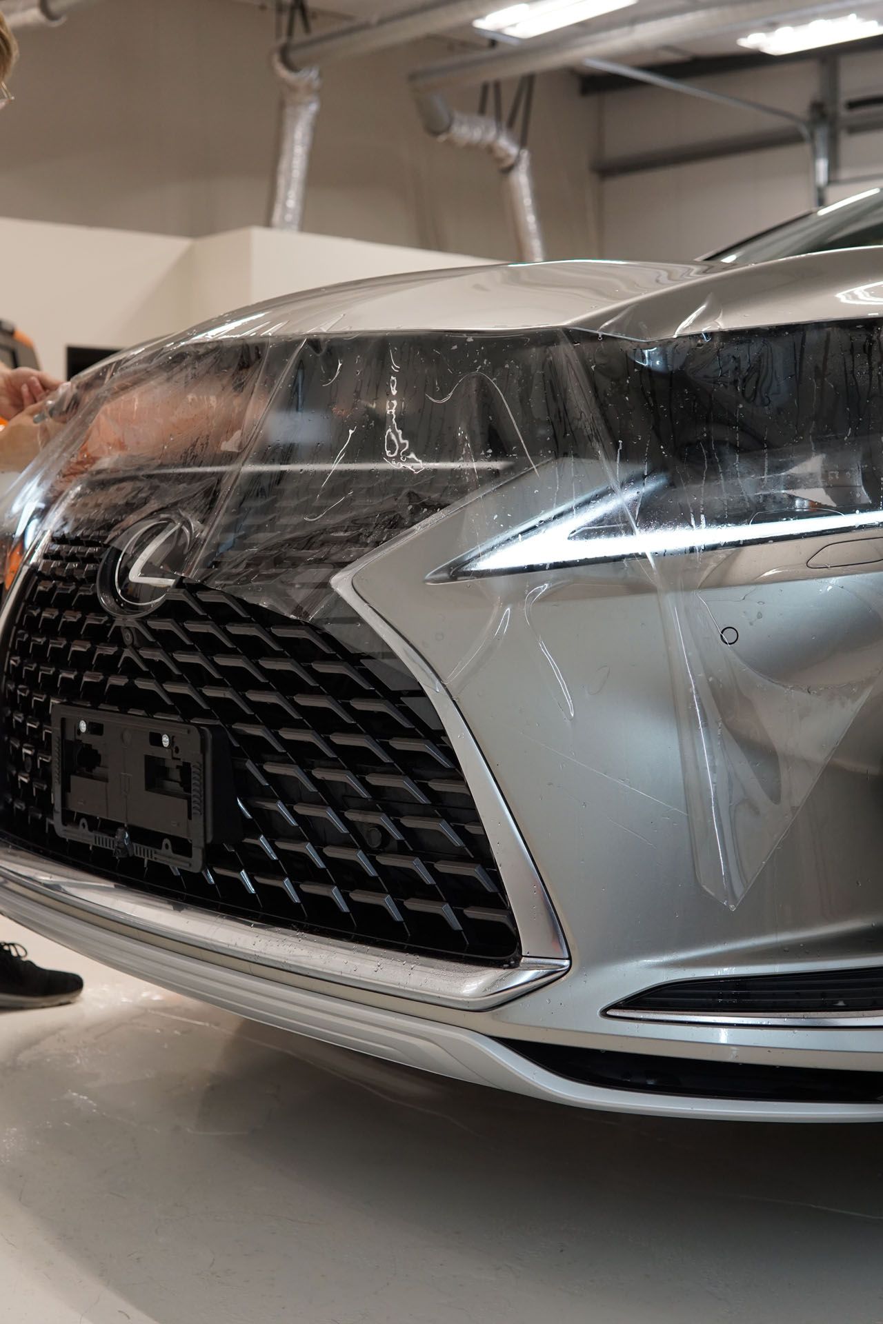Person applying film to a black car fender, using a blue squeegee.