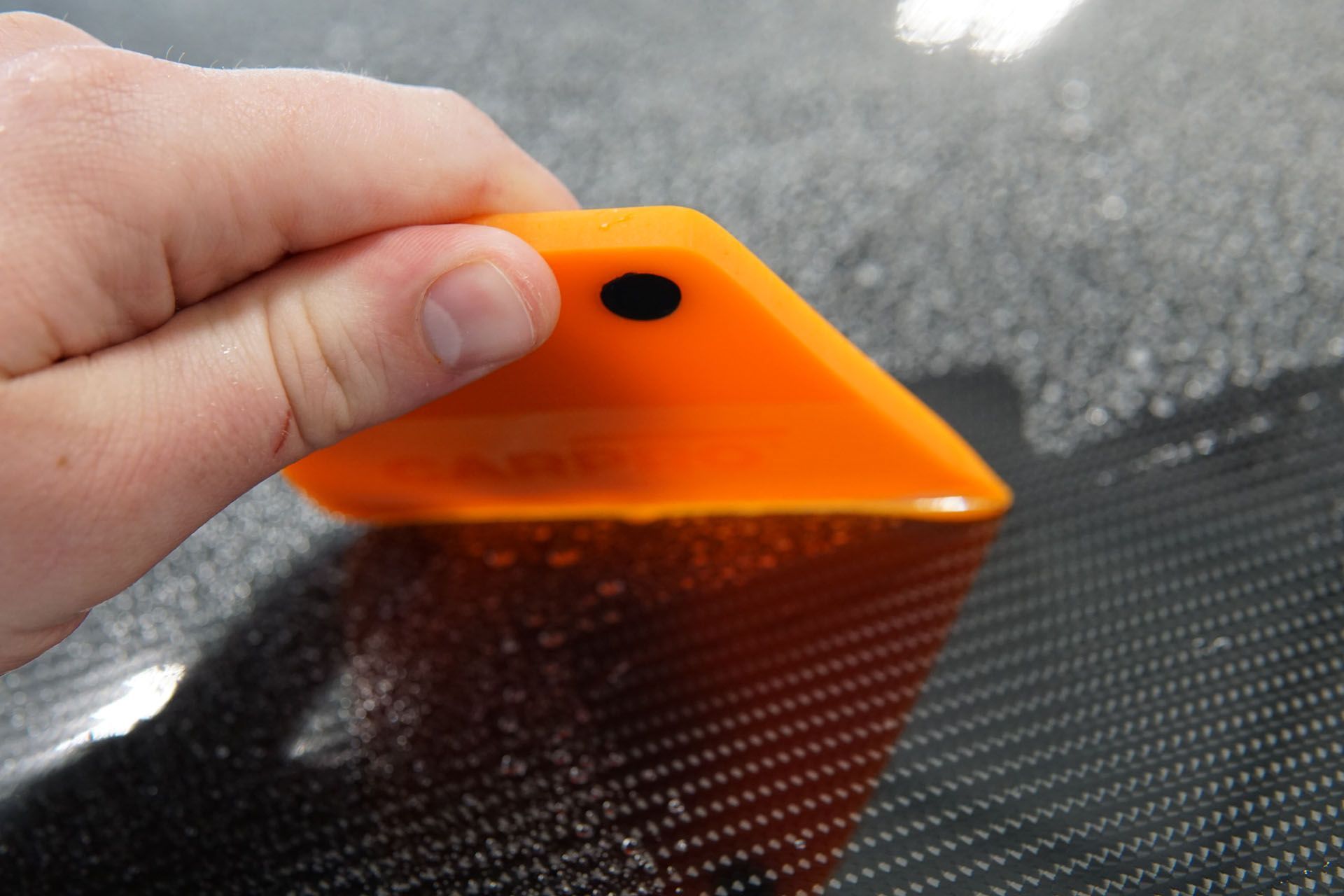 A person is holding an orange squeegee over a black surface.