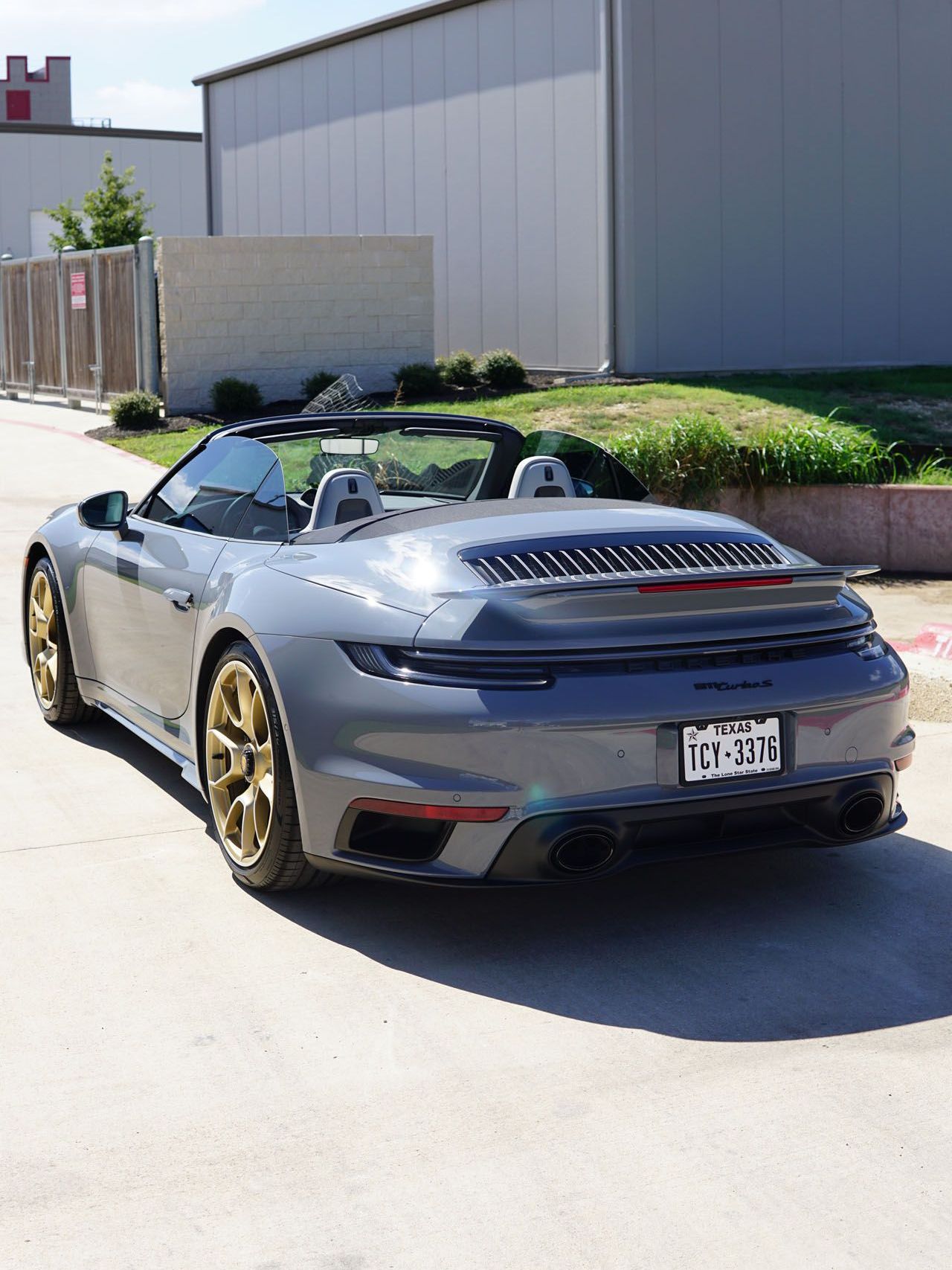 A gray porsche 911 turbo s convertible is parked in front of a building.