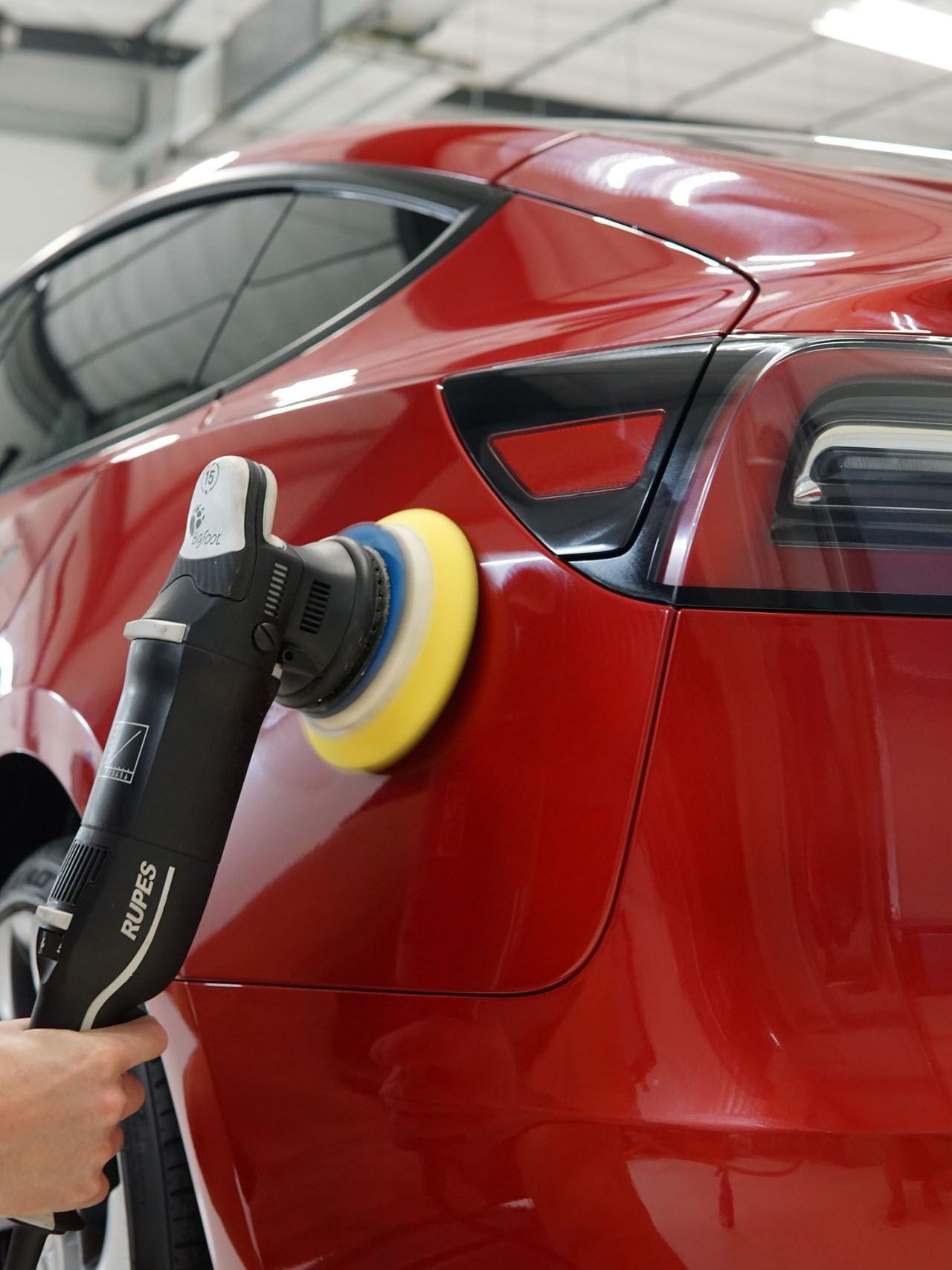 A person is polishing a red car with a machine.