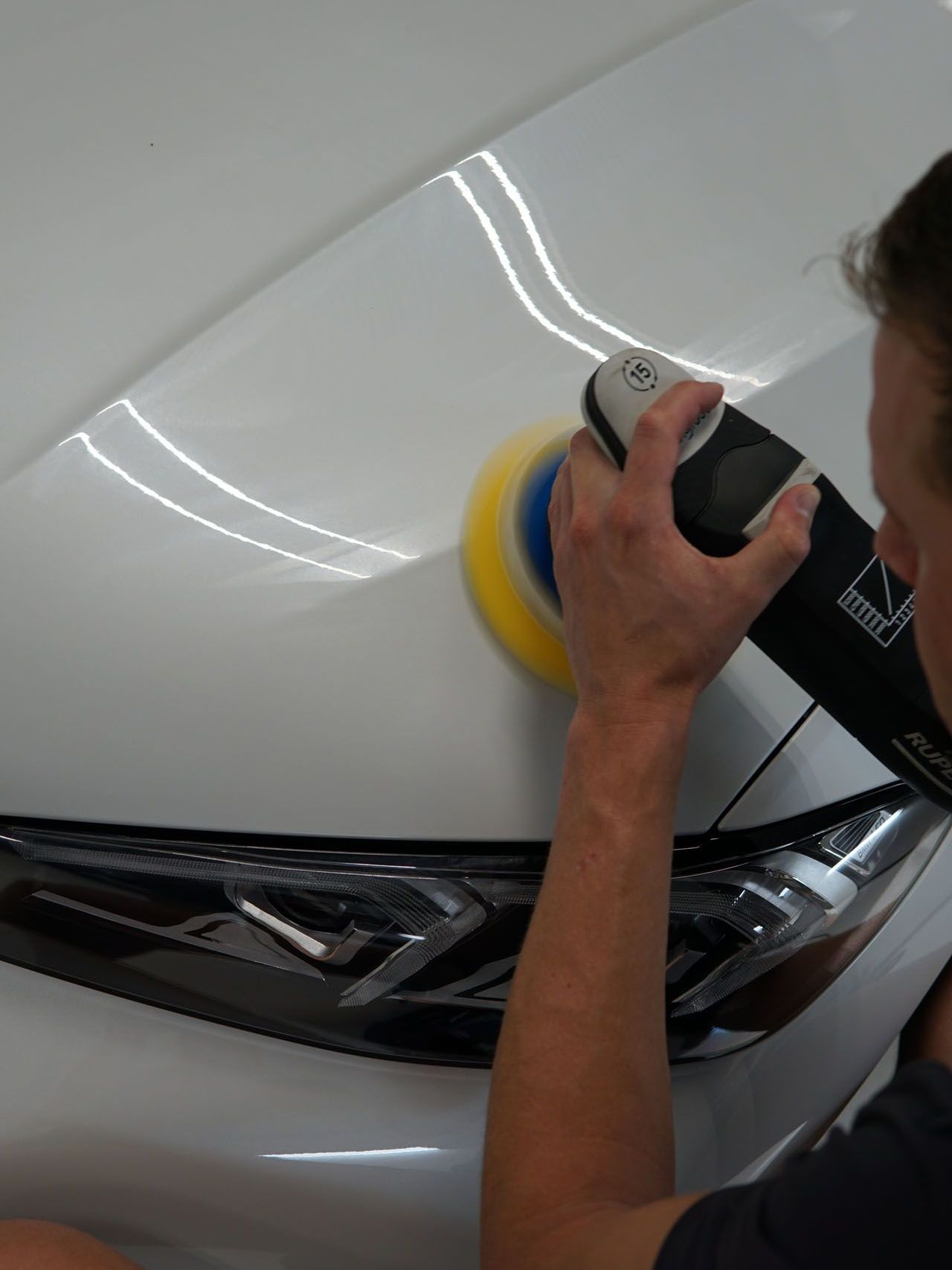 A man is polishing the hood of a white car