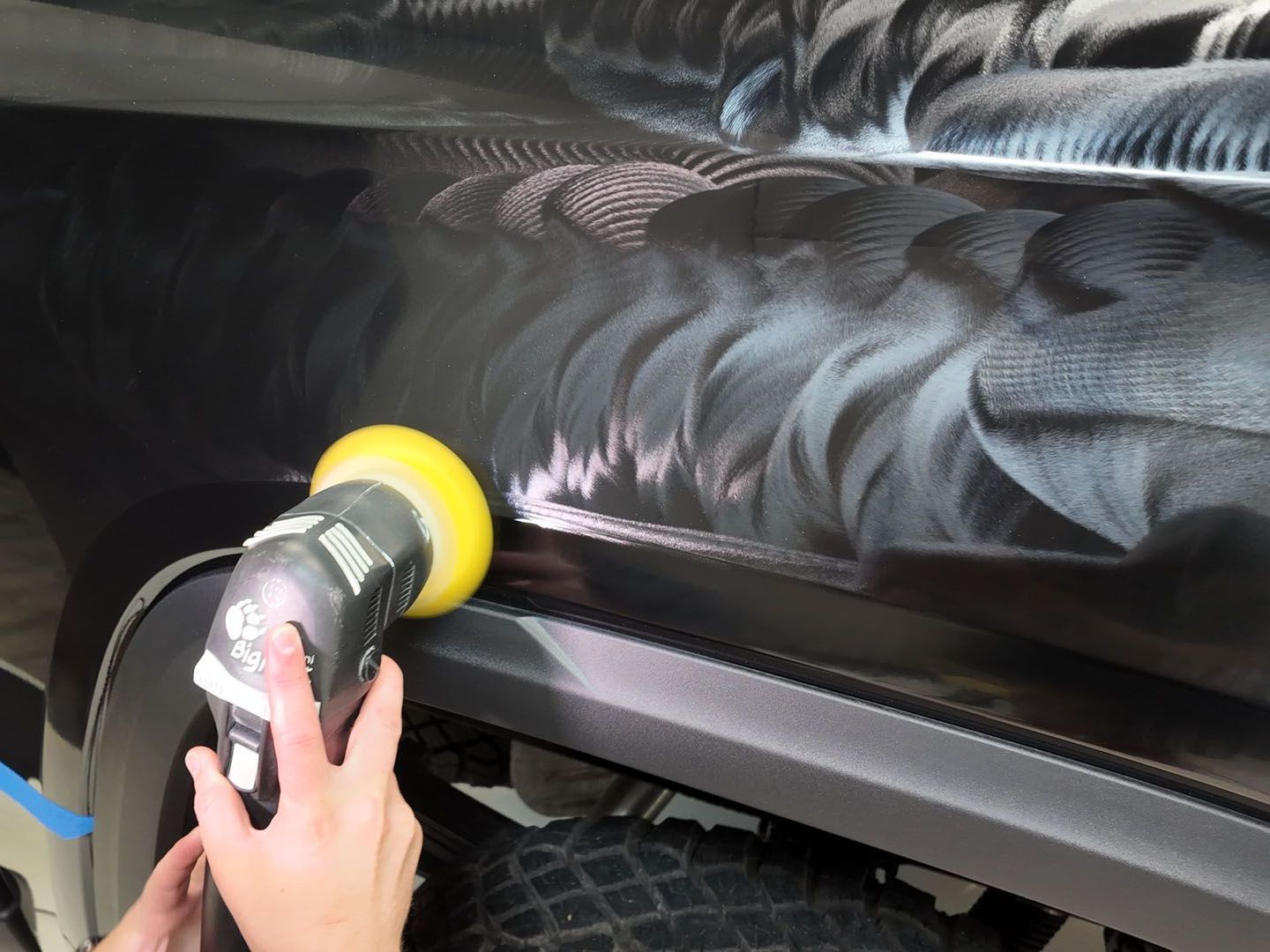 A person is polishing a black car with a yellow polisher