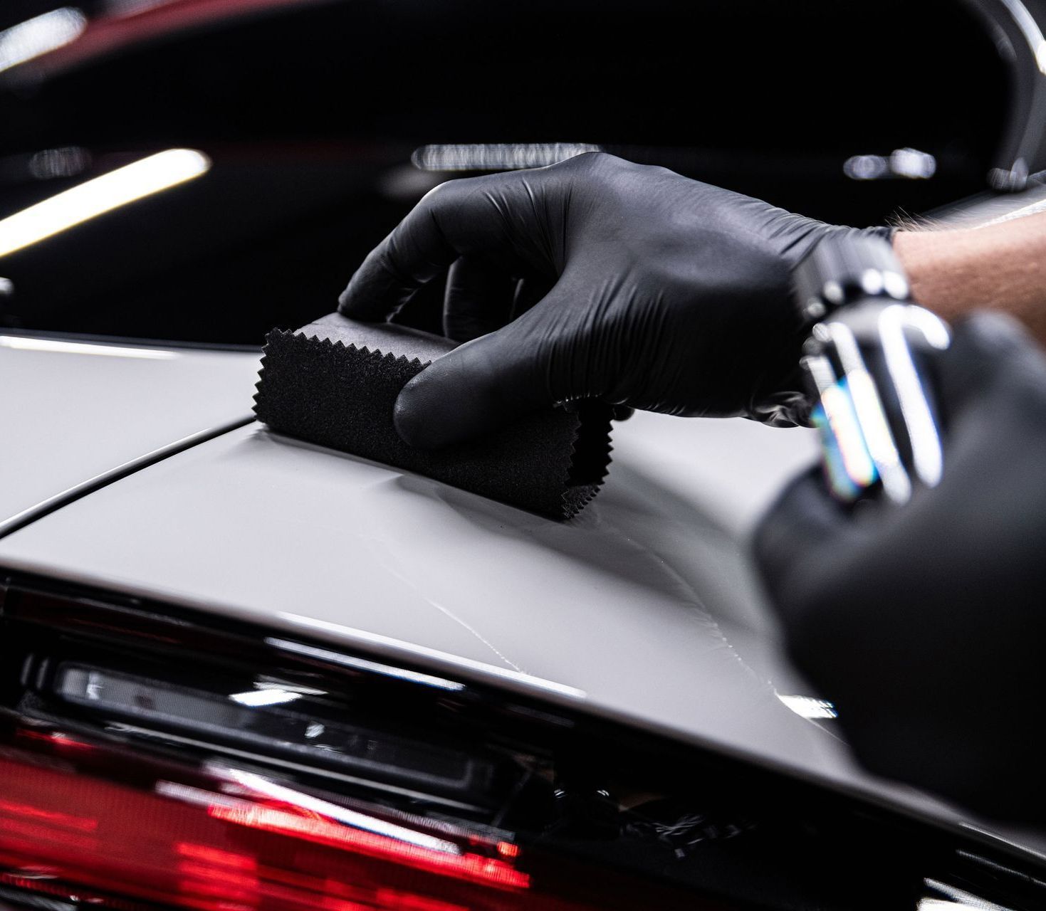 A person wearing black gloves is cleaning a car with a sponge.