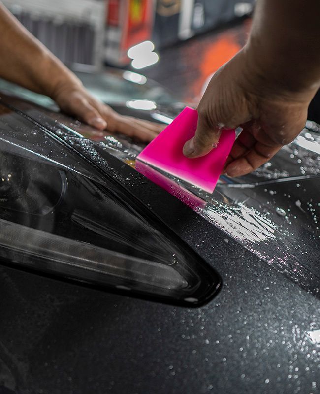 A person is cleaning a car with a pink squeegee.