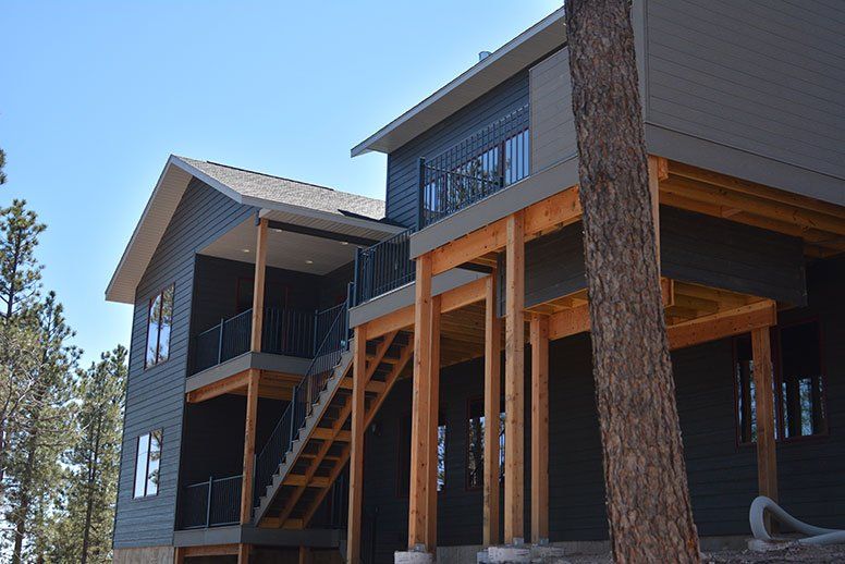 A large house with stairs leading up to the second floor is surrounded by trees.
