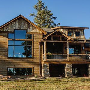 A large wooden house with a lot of windows is sitting in the middle of a grassy field.