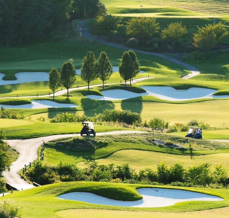 Golf course with green fairways, sand traps, trees, and golf carts on a sunny day.