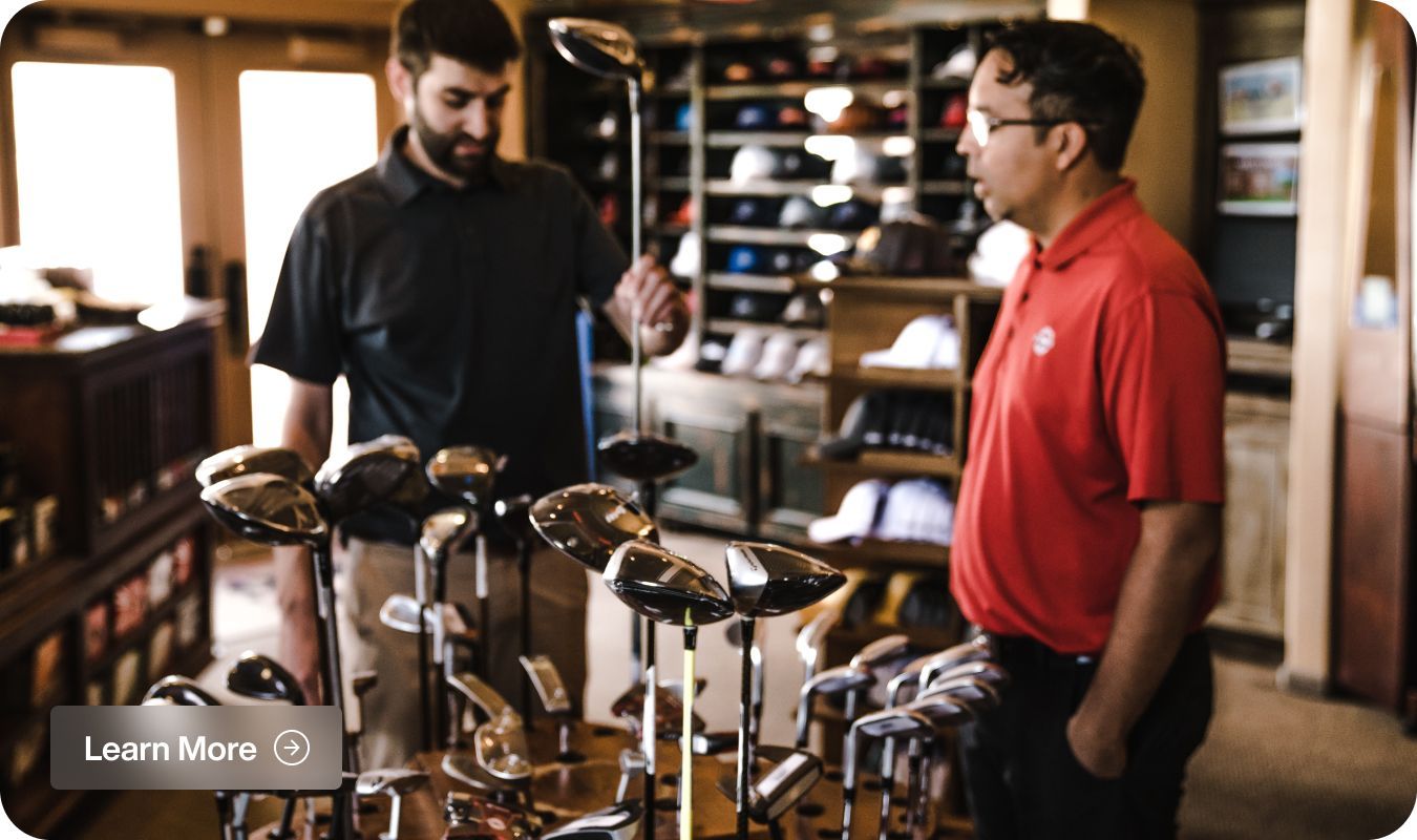 Two men are looking at golf clubs in a store.