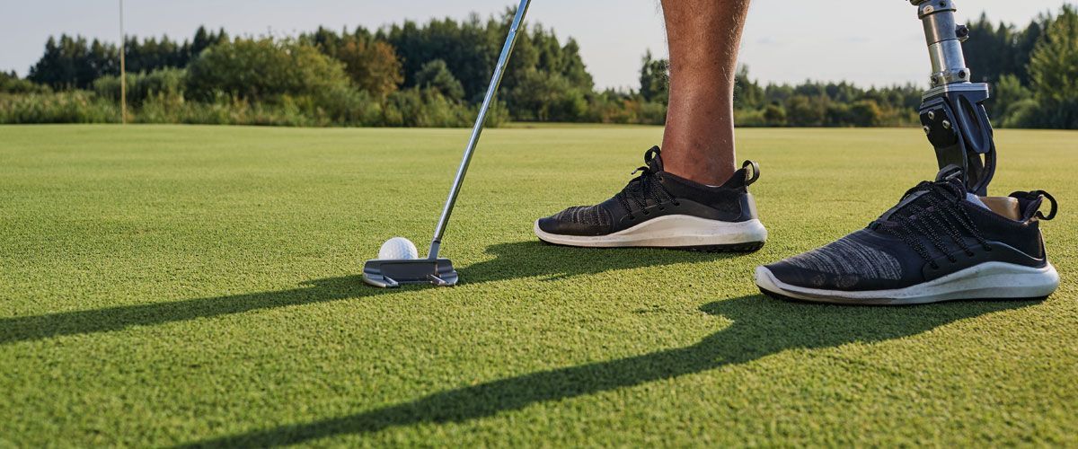 A man with a prosthetic leg is putting a golf ball on a golf course.