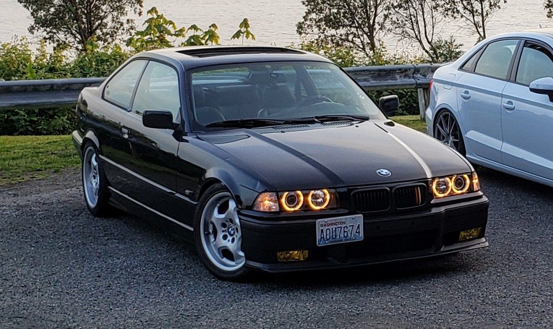 A black bmw is parked next to a white car on a gravel road. | Bavarian Auto Clinic