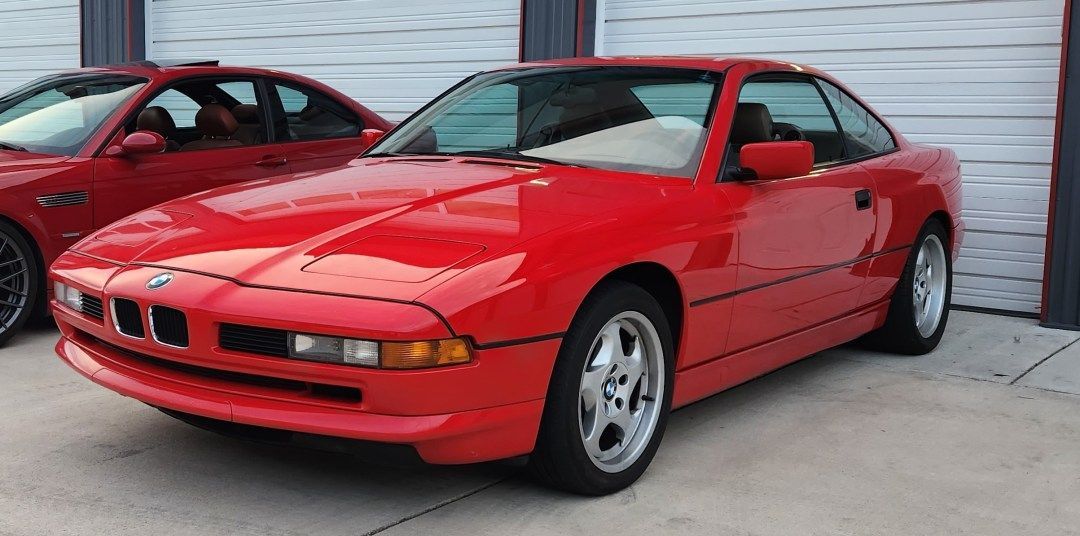 Two red cars are parked next to each other in front of a garage door. | Bavarian Auto Clinic