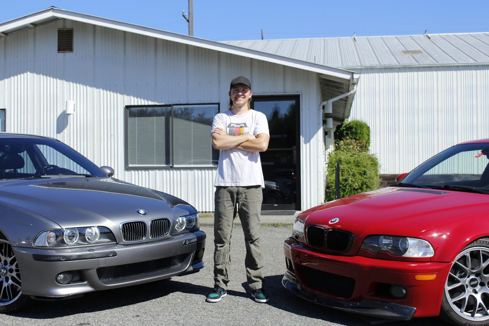 A man is standing next to two cars in front of a building. | Bavarian Auto Clinic