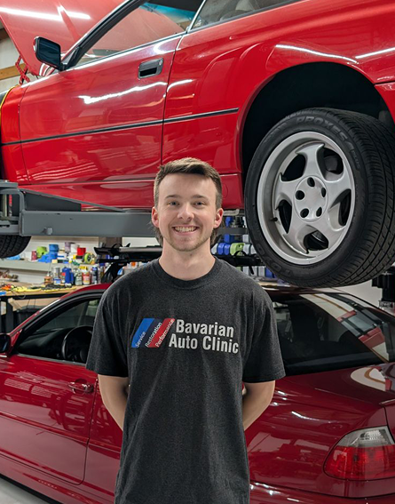 A man wearing a bavarian auto clinic t-shirt is standing in front of a red car. | Bavarian Auto Clinic