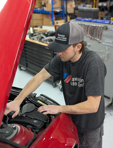 A man is working under the hood of a red car | Bavarian Auto Clinic