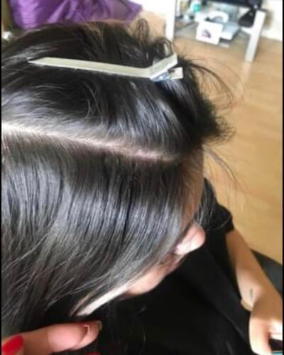 Dark hair parted, clipped with a white barrette; the person's hand is visible.