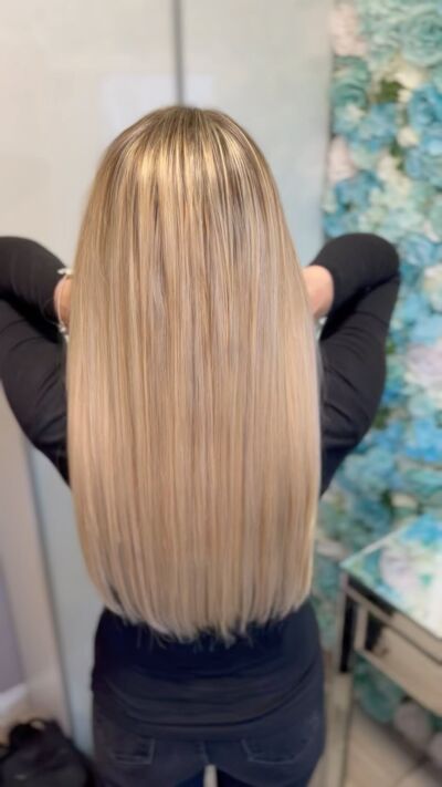 Person with long, straight blonde hair, hands raised near the neck, wearing a black shirt.