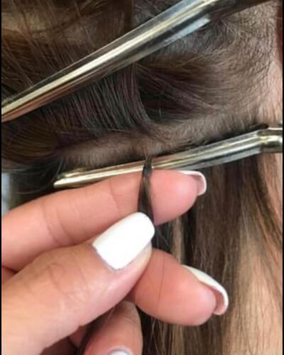 Close-up of a hand holding a strand of hair with hair extensions installed. Silver clips are visible.