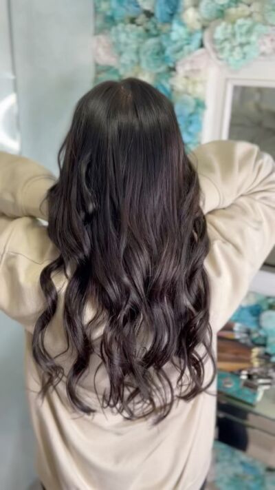 Person with long, wavy dark hair, wearing a light-colored jacket, in a beauty salon.