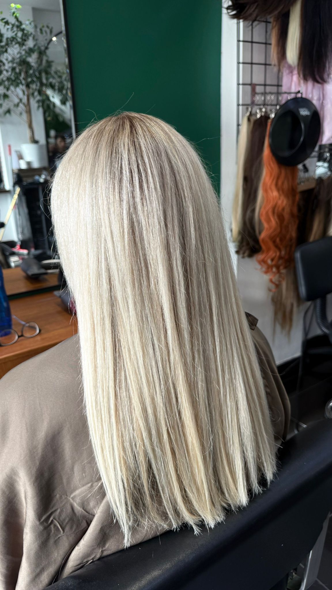 Woman with long, blonde, straight hair; hands behind head. Against a blue-toned wall.
