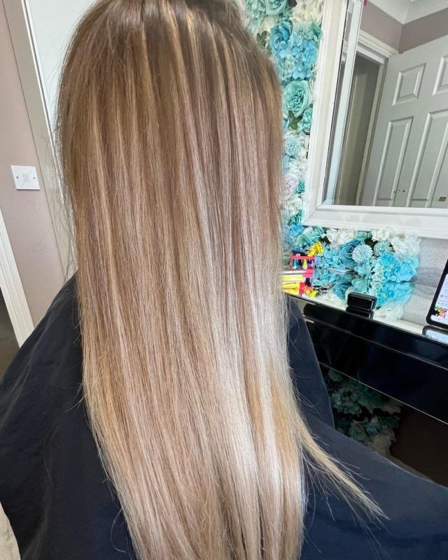 Woman with long blonde hair, highlights, and a gradient effect at a salon.