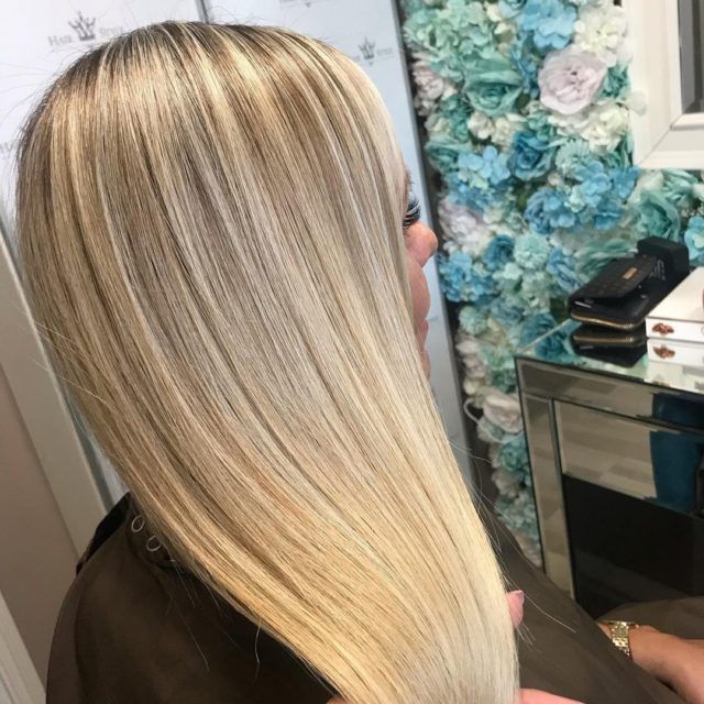 Blonde, straight hair with highlights, styled sleekly. In front of a floral wall and mirror.