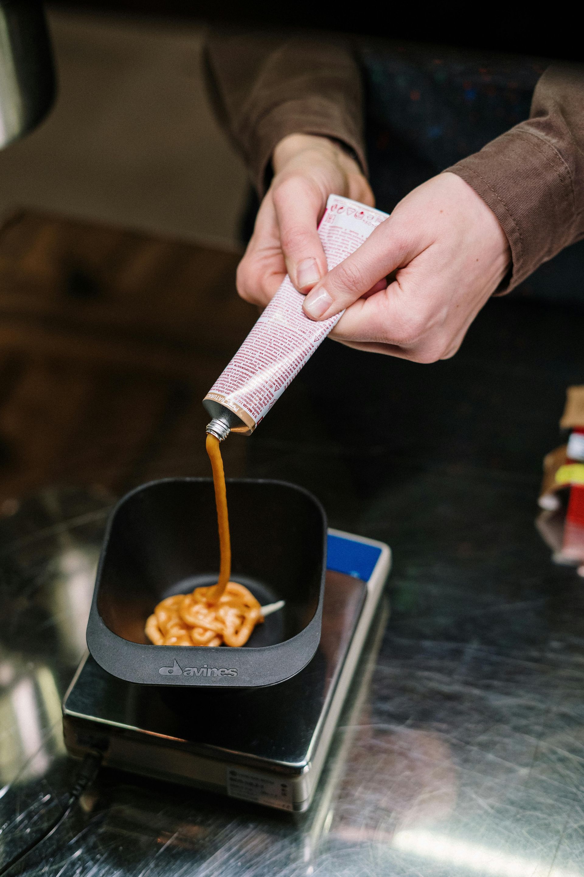 Person squeezing brown liquid from a tube into a black bowl on a scale.
