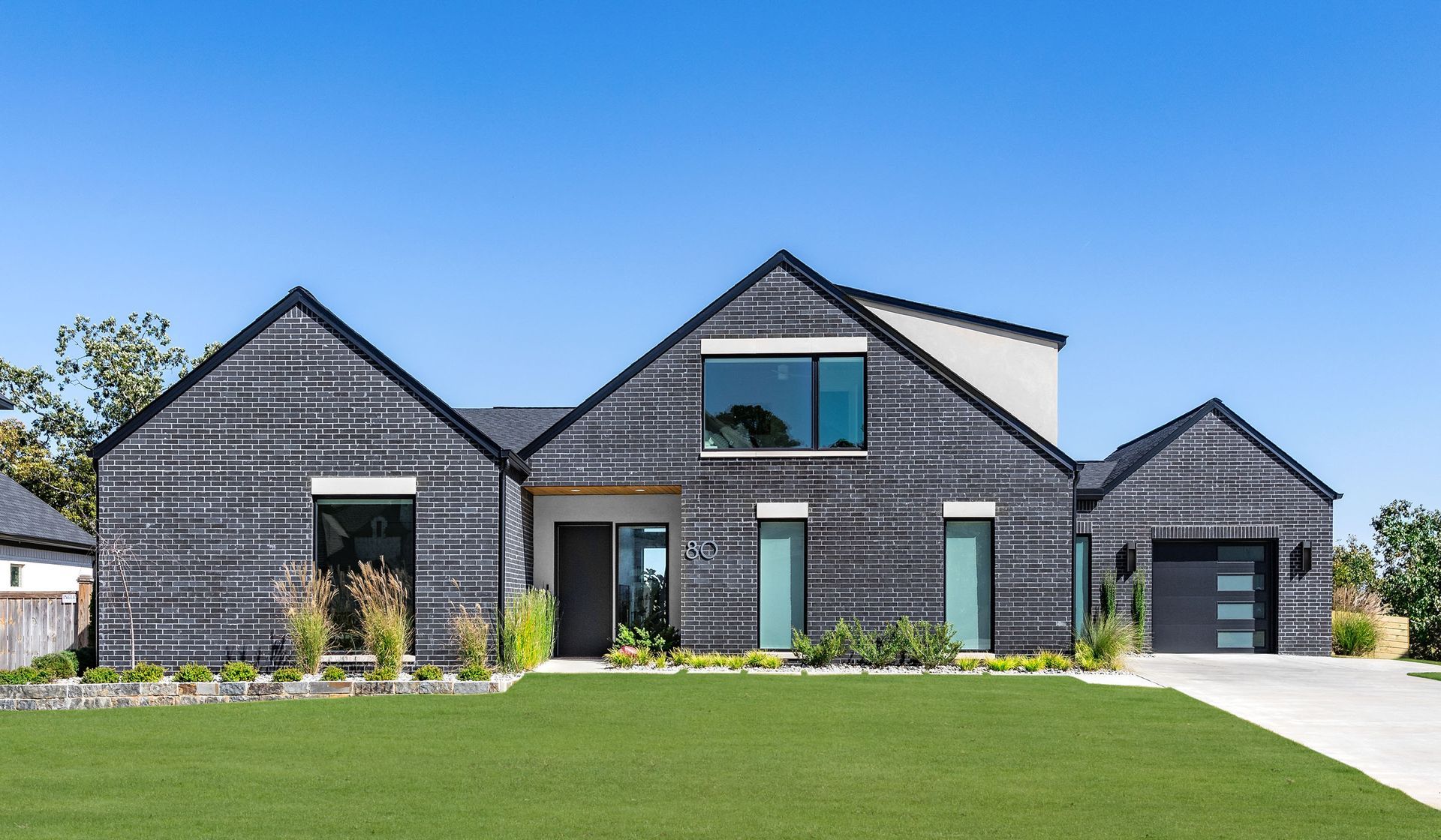 A large black brick house with a lush green lawn in front of it.