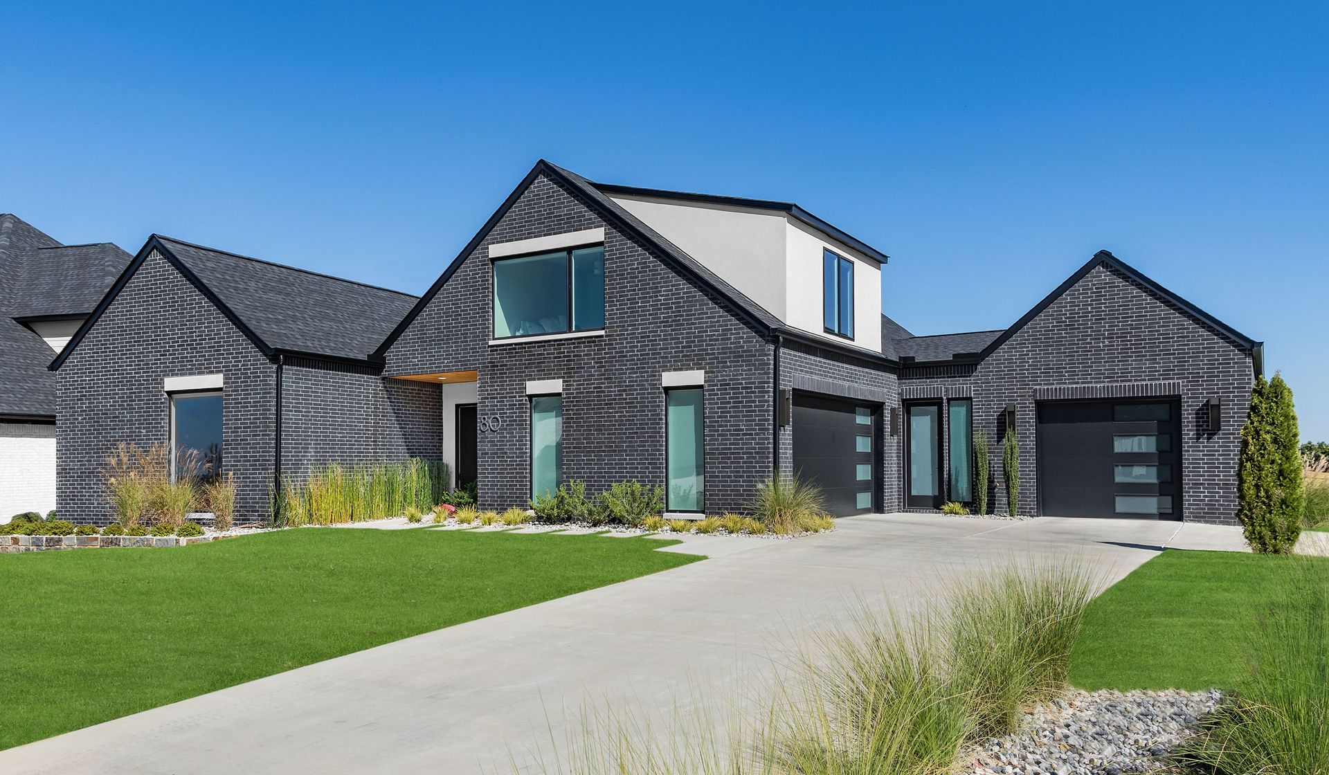 A large black and white brick house with a concrete driveway in front of it.
