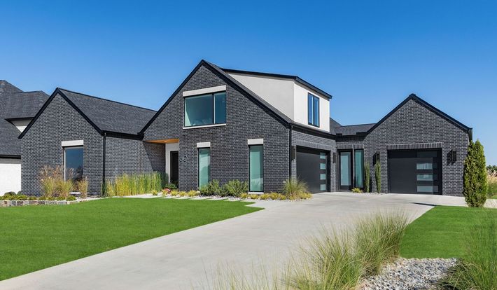 A large black and white brick house with a concrete driveway in front of it.