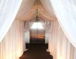 A hallway with white curtains and a chandelier hanging from the ceiling