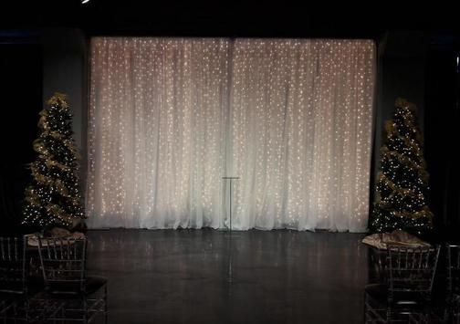 A stage with a white curtain and two christmas trees in front of it.